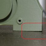 Close-up photo showing first-layer lifting (warping) on an FDM print, highlighted by a red circle, used for a Bambu Studio warping troubleshooting guide.