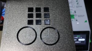 TPU test prints on a textured build plate—square pads and ring-shaped cushions used as anti-slip feet and base cushions for a stand.