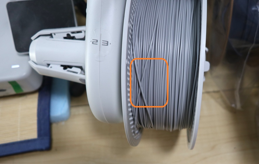 3D printer filament tangled under overlapping windings on a spool attached to Bambu Lab AMS Lite, causing filament feeding problems